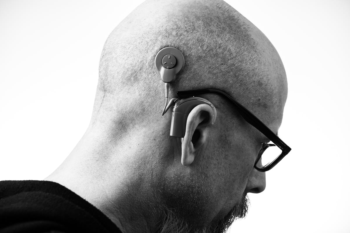 Black and white profile of a man wearing glasses and a hearing aid