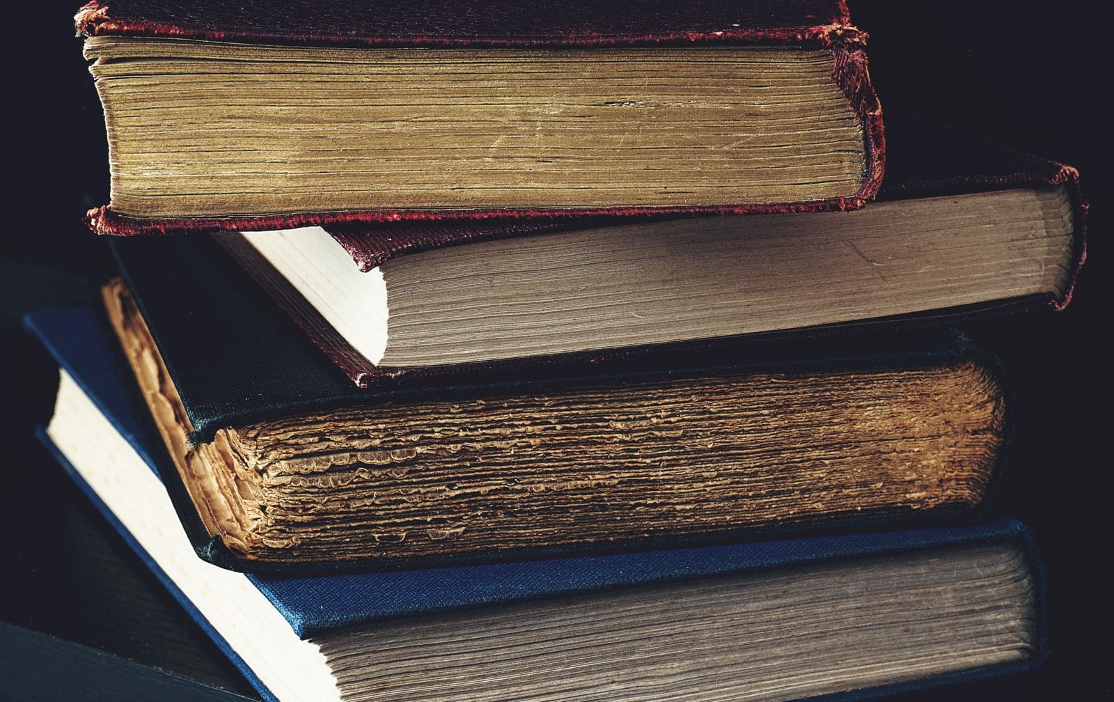 Stack of worn antique hardcover books against a dark background