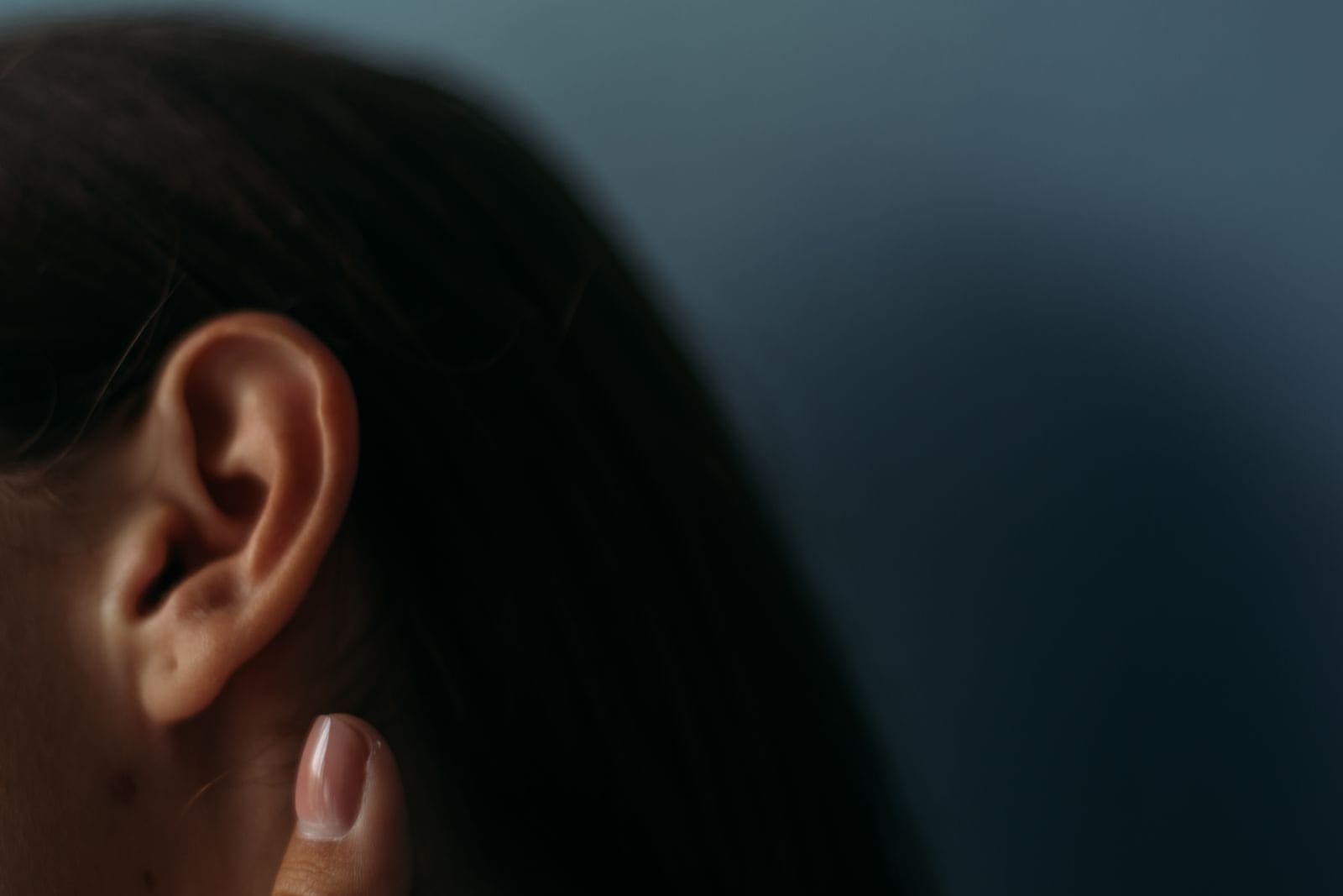 Close-up of a woman's ear with her fingertip resting just below it