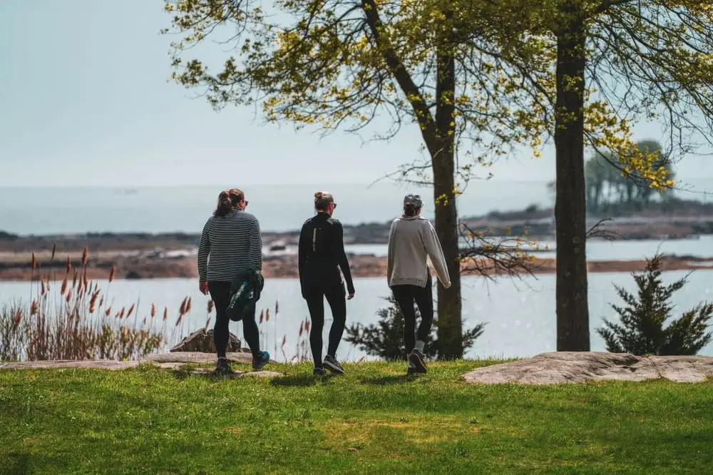 Three women walking together through a sunny lakeside park