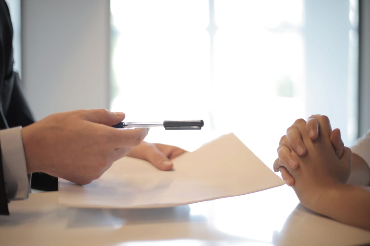 A person handing a pen across a desk to sign a document - protecting your next business idea
