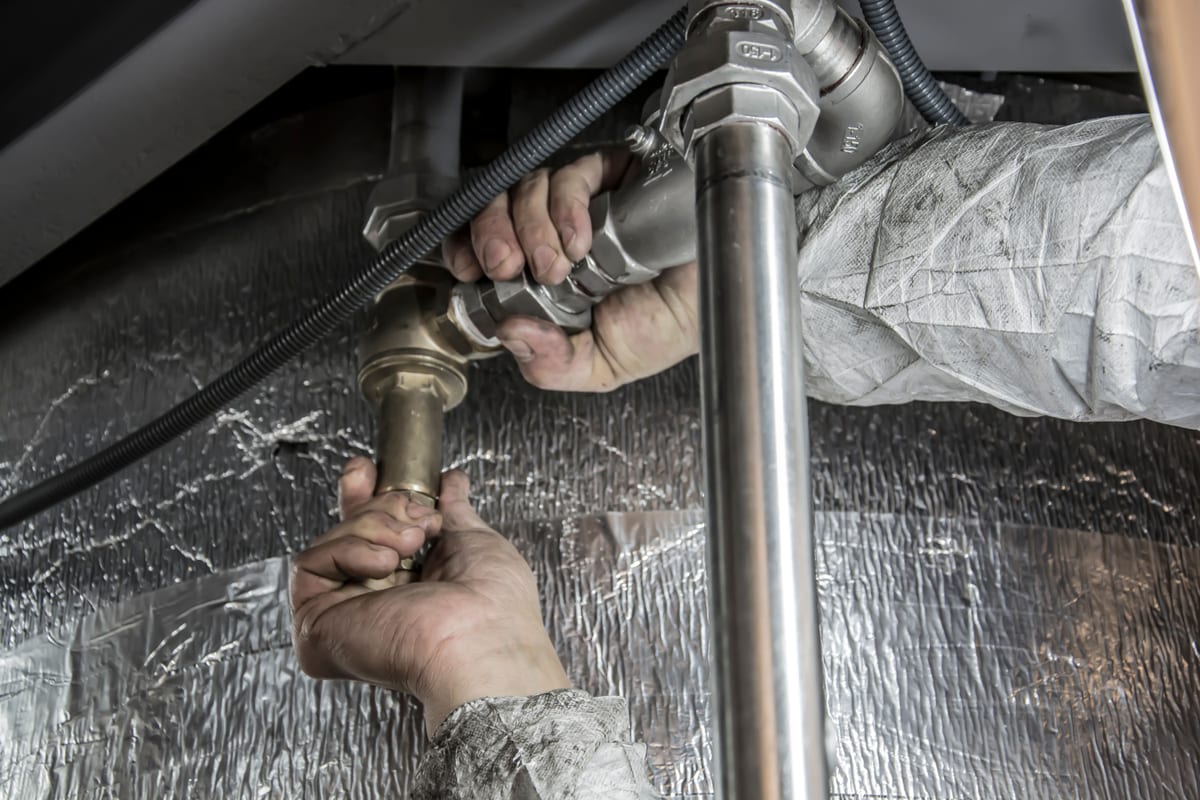 A plumber's hands fitting copper and steel pipes under a sink - spring plumbing maintenance